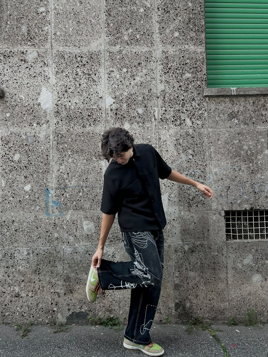 Il ragazzo alza una gamba contro il muro, i disegni bianchi seguono la piega del denim