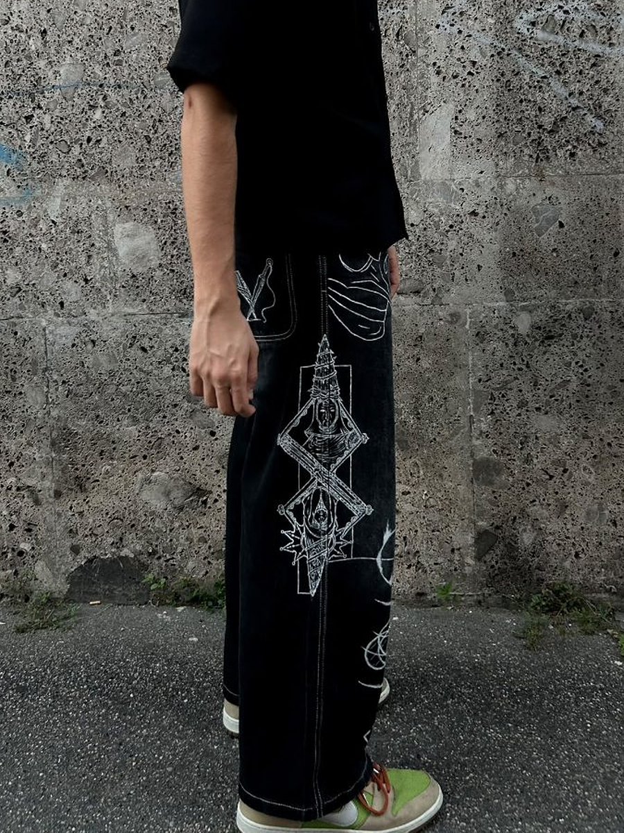 Ragazzo con camicia nera e i jeans neri dipinti, totem e simboli bianchi lungo la gamba